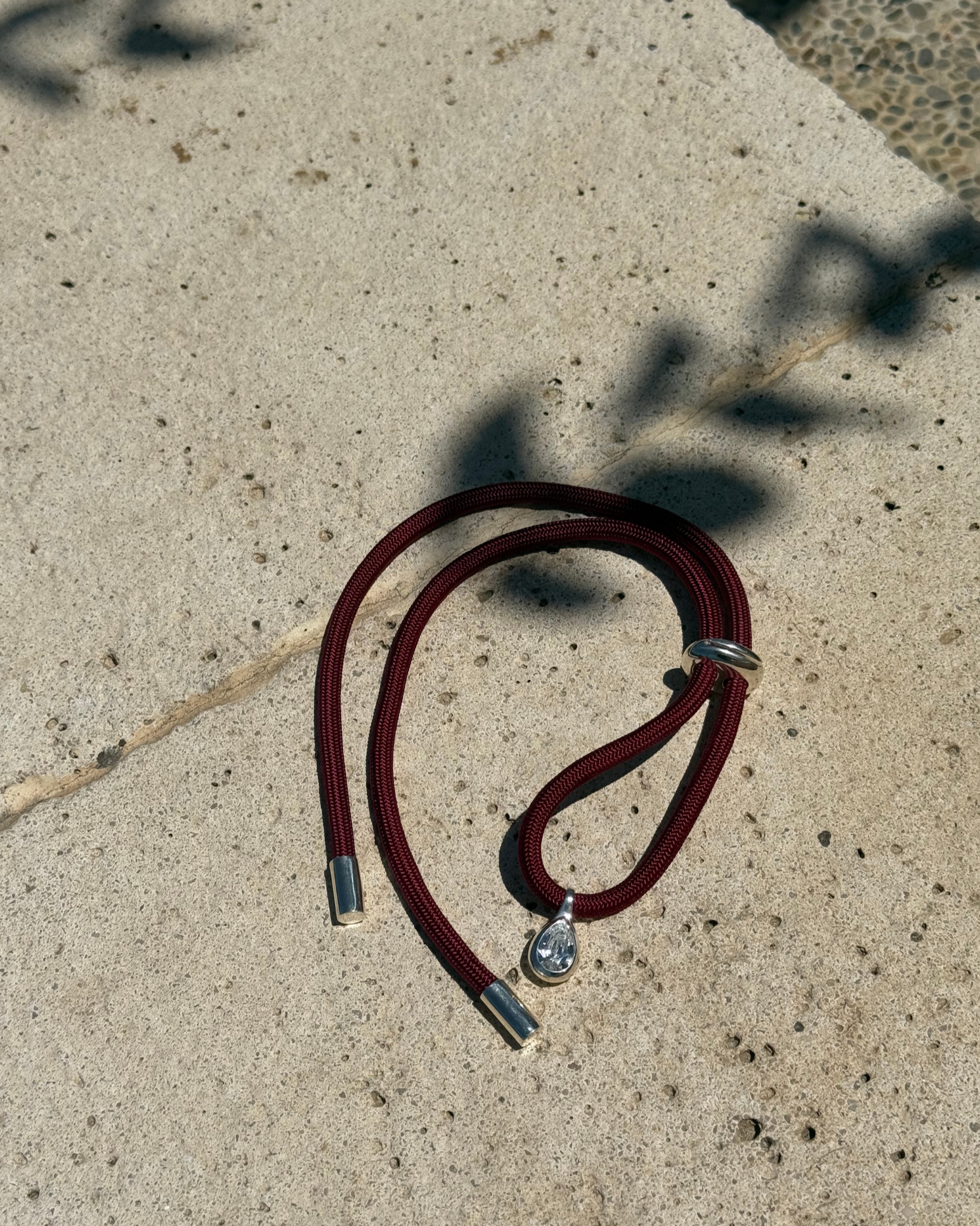 Burgundy cord necklace with silver clasp on a concrete surface