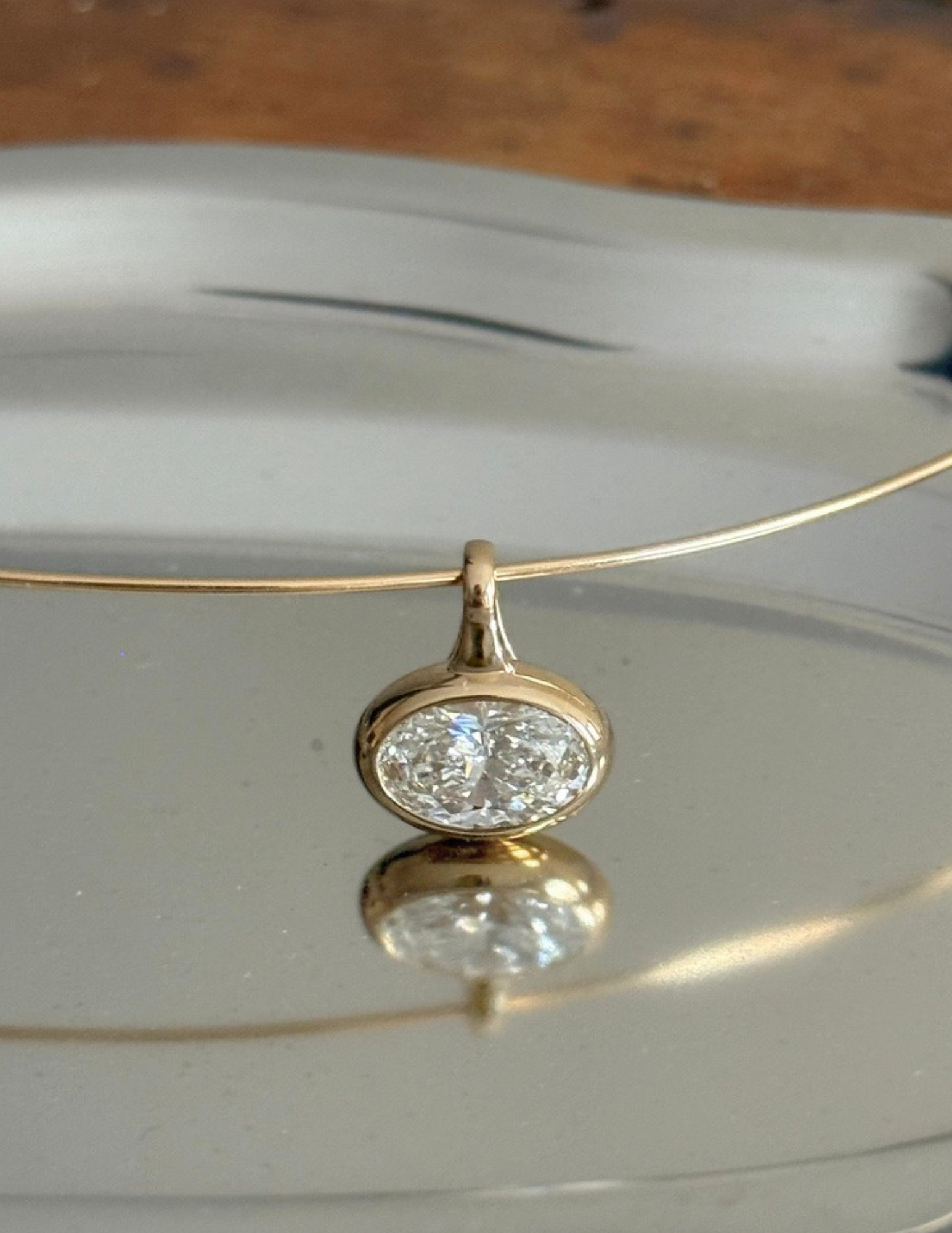Gold necklace with a diamond pendant on a reflective surface